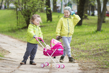 Two children baby girl and boy playing in the yard with a toy stroller.