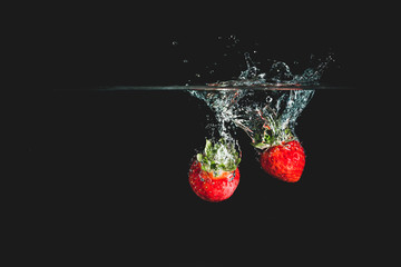 Canvas Print - Two fresh and delicious red strawberries isolated against dark, black background. Red strawberry dropping in water and creating a splash. The concept of healthy eating, consuming fruit.