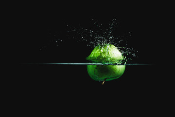 Wall Mural - Fresh and delicious green apple isolated against dark, black background. Green apple dropping in water and creating a splash. The concept of healthy eating, consuming fruit.