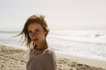 portrait young pretty girl looking on summer beach, hipster in sand coastline on background seascape horizon blue sun ocean, beauty model posing in crochet jacket in nature outdoors