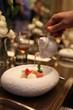 Tableside Service at customer's table by Professional Starred Chef. Pouring over to a luxury fine dining dessert in white stylish bowl. Final touch to perfect meal. Selective focus. Bokeh background. 