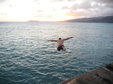 Man Cliff Diving Into The Ocean During Sunset Golden Hour