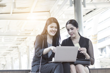 Two happy and funny friends businesswomen  shopping online with credit card and looking on a laptop at outside of working place