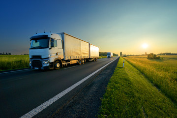 Wall Mural - trucks driving on the asphalt road in a rural landscape in the golden sunset