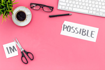 From impossible to possible. Do difficult task at work concept. Cutting the part im of written word impossible by sciccors. Office desk. Pink background top view copy space