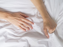 Hand Clutches Grasps A White Crumpled Bed Sheet In A Hotel Room, A Sign Of Ecstasy, Feeling Of Pleasure Or Orgasm. Orgasm Is The Greatest Point Of Sexual Pleasure Or A Climax Of Sexual Excitement