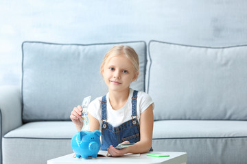 Poster - Little girl putting money into piggy-bank indoors