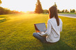 © ViDi Studio - Young female back view. Woman working on laptop pc computer with blank black empty screen to copy space in city park on green grass sunshine lawn outdoors. Mobile Office. Freelance business concept.