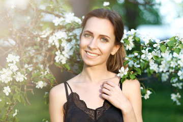 Young beautiful woman enjoying of blooming tree on a sunny day. Portrait of young woman smiling in the flowered garden in the spring time. Almond flowers blossoms. Girl dressed in white like a bride