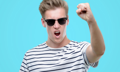 Sticker - Young handsome blond man wearing sunglasess annoyed and frustrated shouting with anger, crazy and yelling with raised hand, anger concept