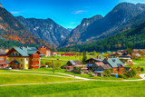 Fototapeta Tęcza - Alpine green fields and traditional wooden houses view of the Gosau village at autumn sunny day.