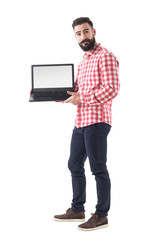 Wall Mural - Cool bearded hipster guy in smart casual clothes showing blank laptop monitor. Full length isolated on white background. 