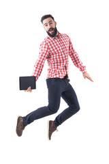 Wall Mural - Successful excited young business man holding tablet jumping in mid air with open mouth. Full length isolated on white background. 