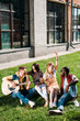 interracial group of friends with acoustic guitar resting on green grass on summer day
