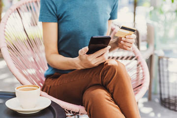 Wall Mural - Young woman holding credit card and using smartphone. Travel, vacations and online shopping concept