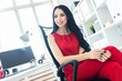 © Ivan Traimak - Beautiful young girl in a red suit is sitting in a chair in the office.
