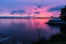Colorful Pink, Purple & Blue Sunset Over A Calm Lake With A Pontoon Boat At The Shore. Beautiful Northwoods Scene With A Colorful Sky Reflected In The Water. Concepts Of Vacation, Nature, Travel