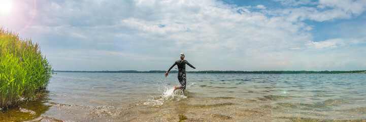 Wall Mural - Triathlete runs into the Cospudener Lake near Leipzig to swim, panorama