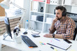 © Ivan Traimak - A young man in headphones sits at a table in the office and looks at the monitor.