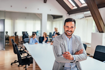 Wall Mural - Handsome executive smiling in the office, with colleagues in background.