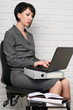© soleg - business woman with laptop and folders, dressed in a gray suit poses in front of a white wall