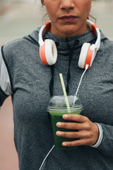 Wall Mural - Healthy sport and fitness nutrition concept. Woman drinking green detox smoothie during workout rest.