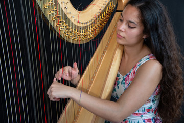 Close-up of a beautiful girl with long brown hair playing the harp. Detail of a woman playing the harp