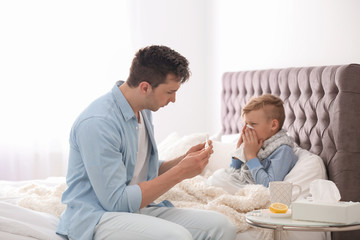 Canvas Print - Father taking care of little son suffering from cold in bed