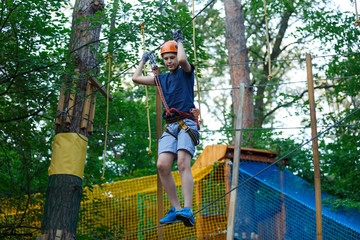 Active sporty kid in helmet doing activity in adventure park with all climbing equipment. Active children climb on the trees and having fun outdoors. Summer camp.