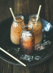 Wall Mural - Refreshing summer drink. Cold Thai iced tea in bottles with milk on plate over dark wooden background, selective focus. Vegetarian, healthy food concept