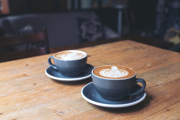 Closeup image of two blue cups of hot latte coffee with latte art on vintage wooden table in cafe