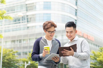 two smiling male work coworkers outdoors talking together over a digital tablet