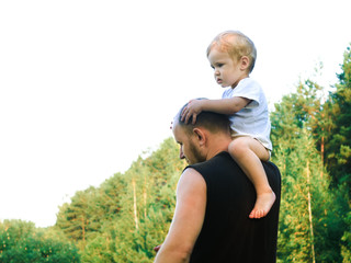a little boy climbed onto his father's shoulder and sits there like a parrot. father plays with his 