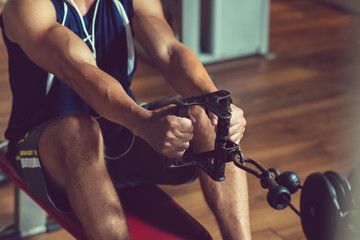 Close-up shot of young muscular man doing exercise on rowing machine at modern gym while having intensive workout