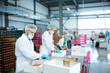© Seventyfour - Confectionery factory workers in white coats collecting freshly baked pastry into paper boxes.