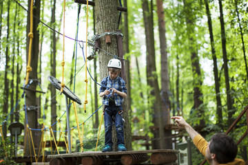 Wall Mural - boy enjoys climbing in the ropes course adventure. smiling child engaged climbing high wire park.