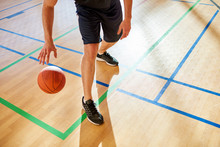 Crop Basketball Player Dribbling Ball On Court Floor During Match. 