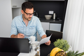 Handsome man using laptop computer at home, drinking juice and coffee in the morning. Working From Home.