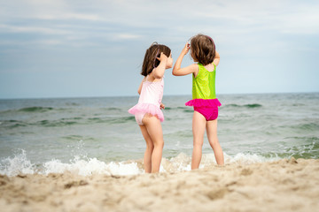 two little girls sisters are standing and playing on the sand at the beach on a summer day