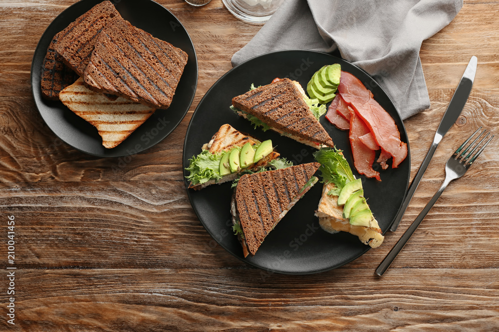 Plate with delicious sandwiches on wooden table