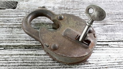 old rusty padlock with key on white wooden surface. close-up. key in keyhole