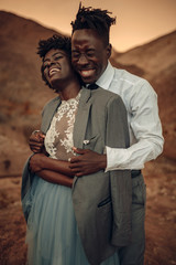 Wall Mural - Groom hugs his bride dressed in his jacket in canyon at sunset and they laugh cheerful.