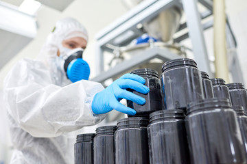 Sports nutrition production worker standing in protective clothing and taking black jar from pile.