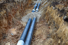 Black Steel Pipes Of The Water Pipeline In The Excavated Earth Ditch
