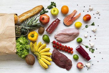 Top view, paper bag of different healthy products over white wooden background. Healthy food concept.