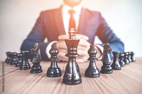 Fotomural Retro style image of a businessman with clasped hands planning strategy with chess figures on an old wooden table