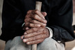 Asian old man sitting with his hands on a walking stick
