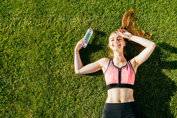 Portrait of a happy young fitness woman laughing and resting on grass after workout and smiling. Sport in open air and health care concept.