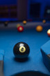 Black billiard ball close to hole over blue felt