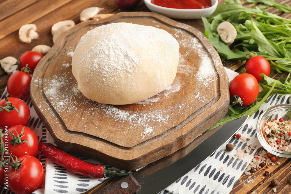 Composition with raw dough and ingredients for pizza on wooden background